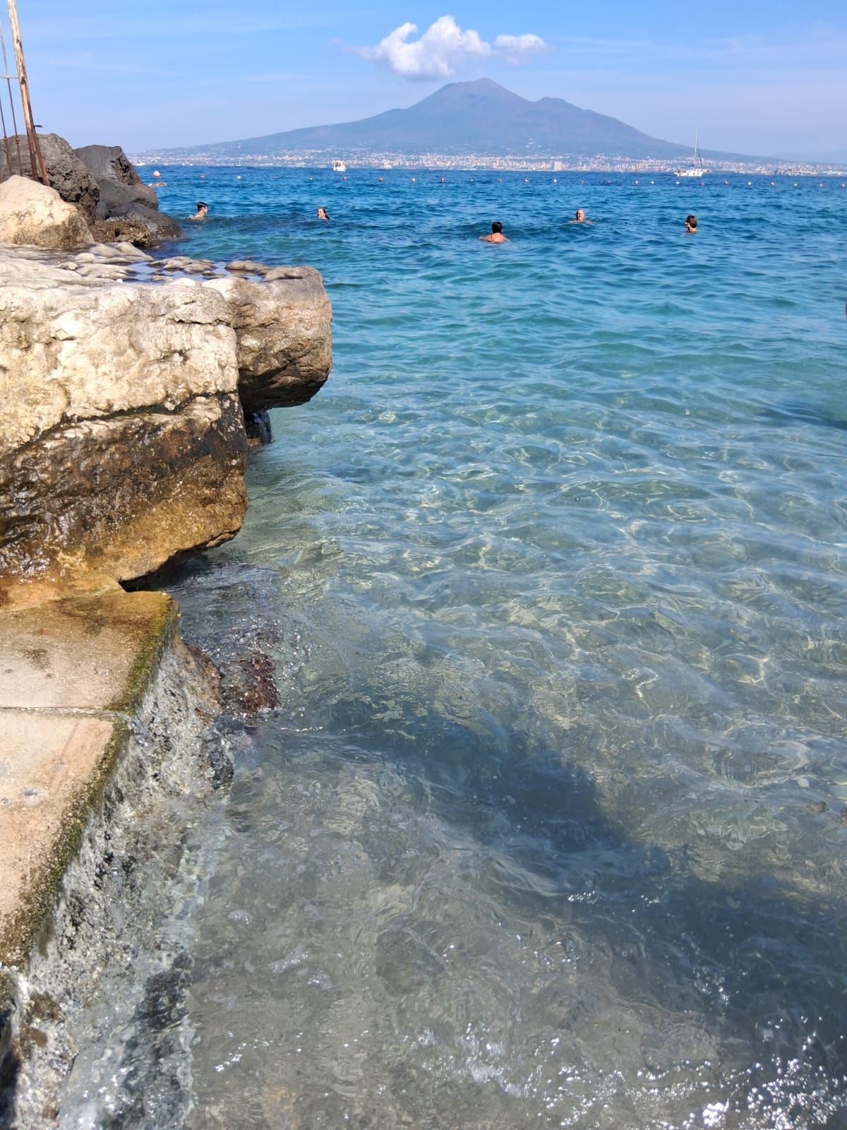 A coastal scene with clear water, rocky shore, and a distant mountain.