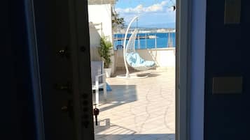 An open door leading to a balcony with a view of the sea, a hanging chair, and a tiled floor.