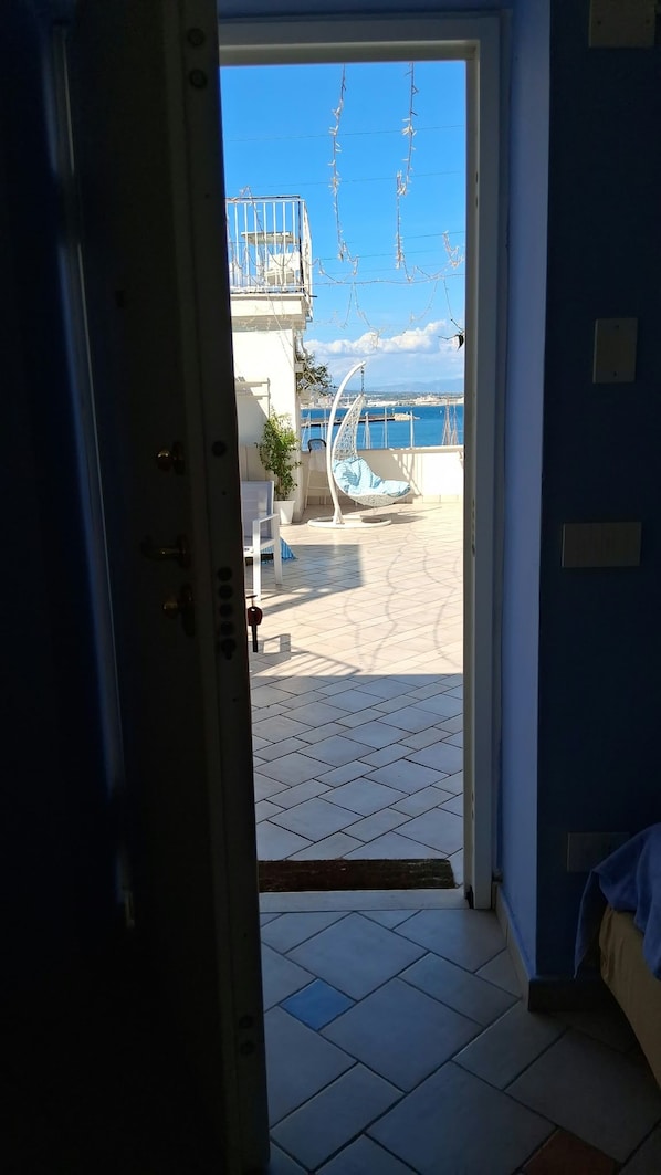 An open door leading to a balcony with a view of the sea, a hanging chair, and a tiled floor. - Coralinetiny (Castellammare di Stabia)