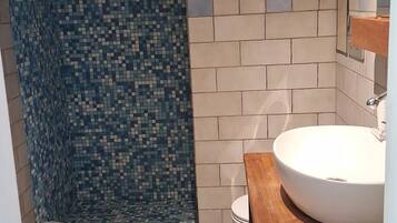 Une salle de bain avec un sol carrelé, un lavabo blanc et un espace douche aux carreaux de mosaïque bleus.