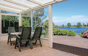 Ein Wintergarten mit Tisch und Stühlen, mit Blick auf einen See, Bäume und einen klaren Himmel.