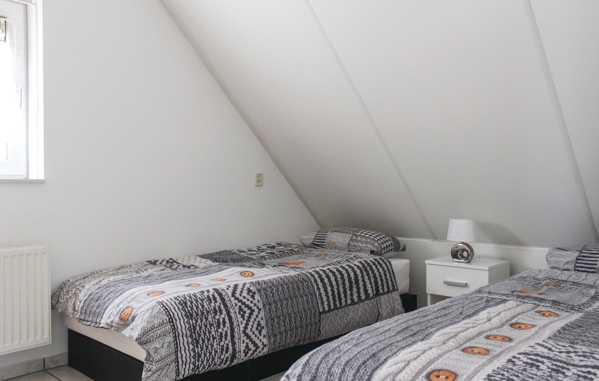 A bedroom with a sloped ceiling, a bed with patterned bedding, a bedside table, and a nightstand.