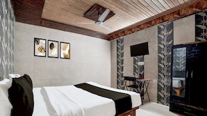 Una camera da letto con un letto, una ventola a soffitto, una TV a schermo piatto montata a parete e opere d'arte incorniciate sopra il letto.