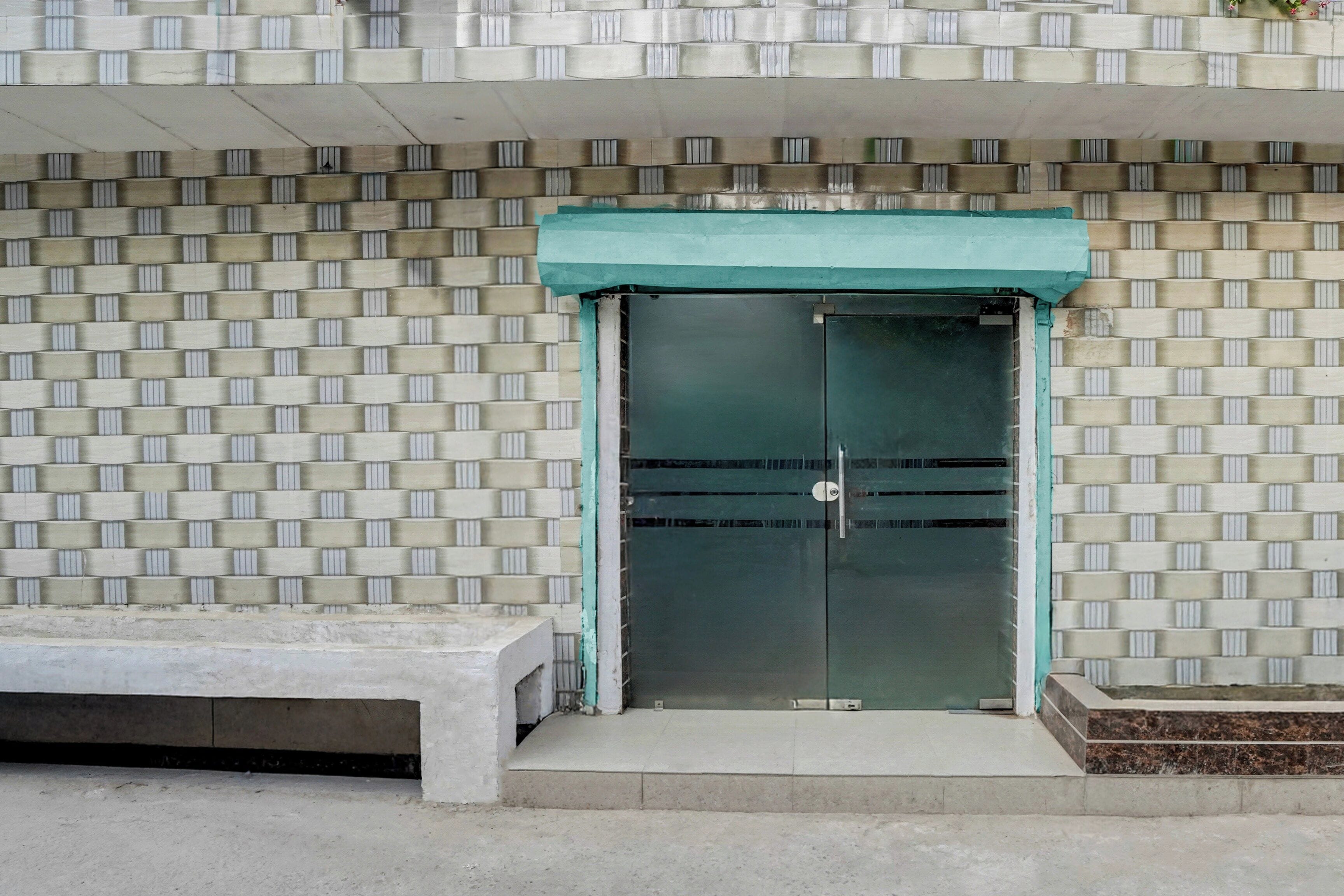 A building entrance with a patterned wall, a green awning, and a bench.