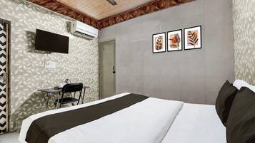 A hotel room with a bed, a desk with a chair, a television, and three framed pictures on the wall.