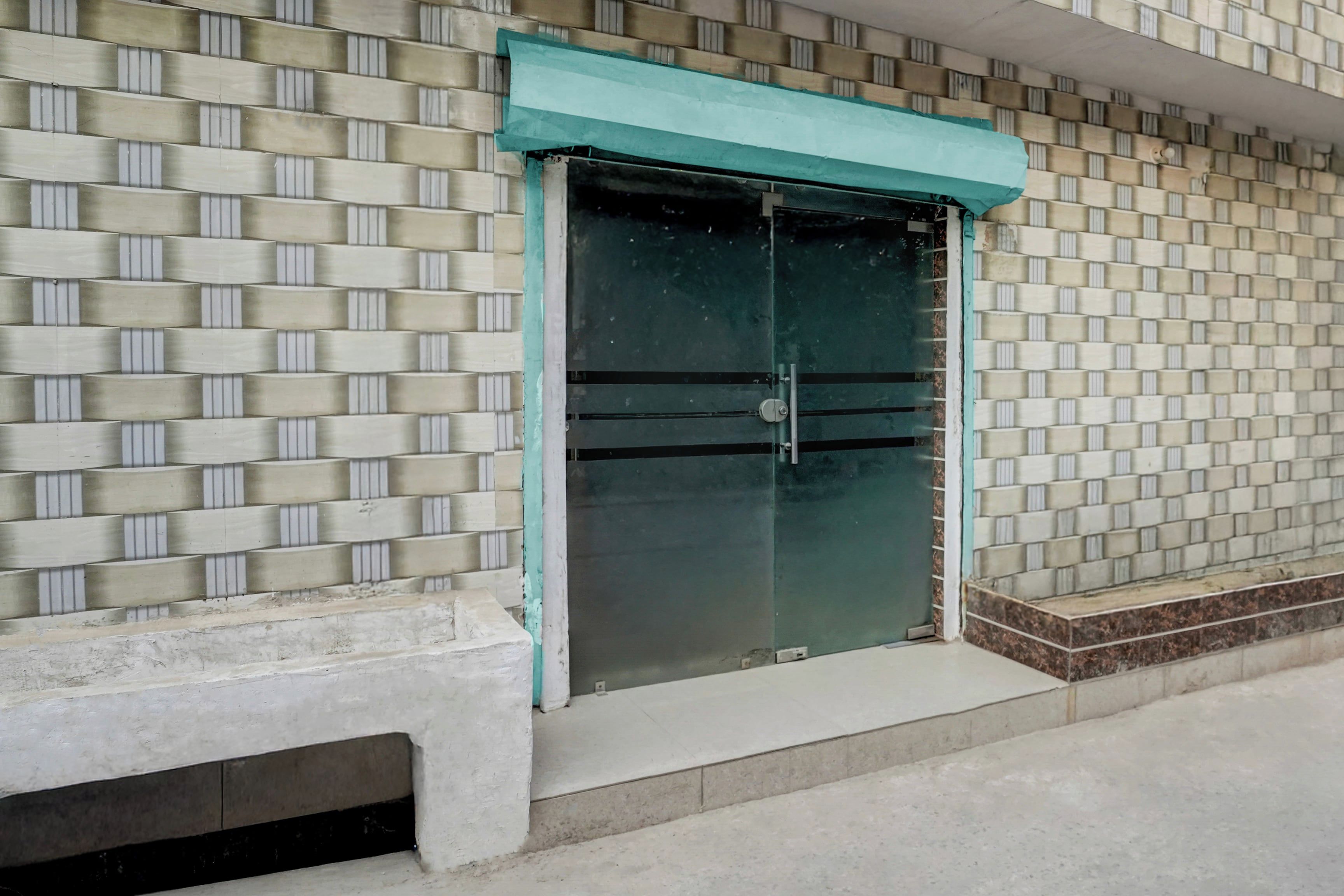 A building facade with a patterned brick wall and a large glass door with a teal awning.