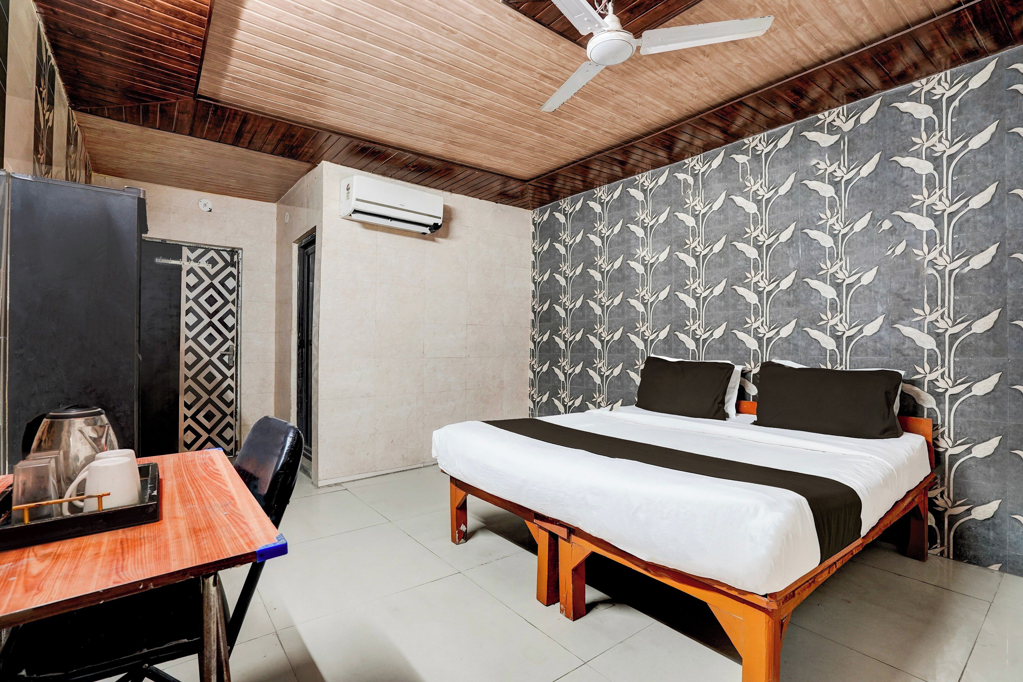 A bedroom with a bed, a desk, a chair, a ceiling fan, and an air conditioning unit.
