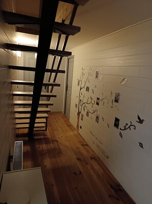 Eine Treppe mit Holzdielen und einem Metallgeländer, die zu einem Raum mit weißen Wänden führt, der mit gerahmten Bildern und einer Baummalerei verziert ist.
