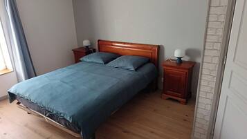 A bedroom with a wooden bed, two bedside tables with lamps, a window with curtains, and a brick-patterned wall.
