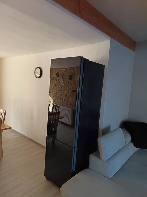 Ein kompakter Wohnraum mit einem schwarzen Kühlschrank, einer Couch, einem Esstisch mit Stühlen und einer Wanduhr.