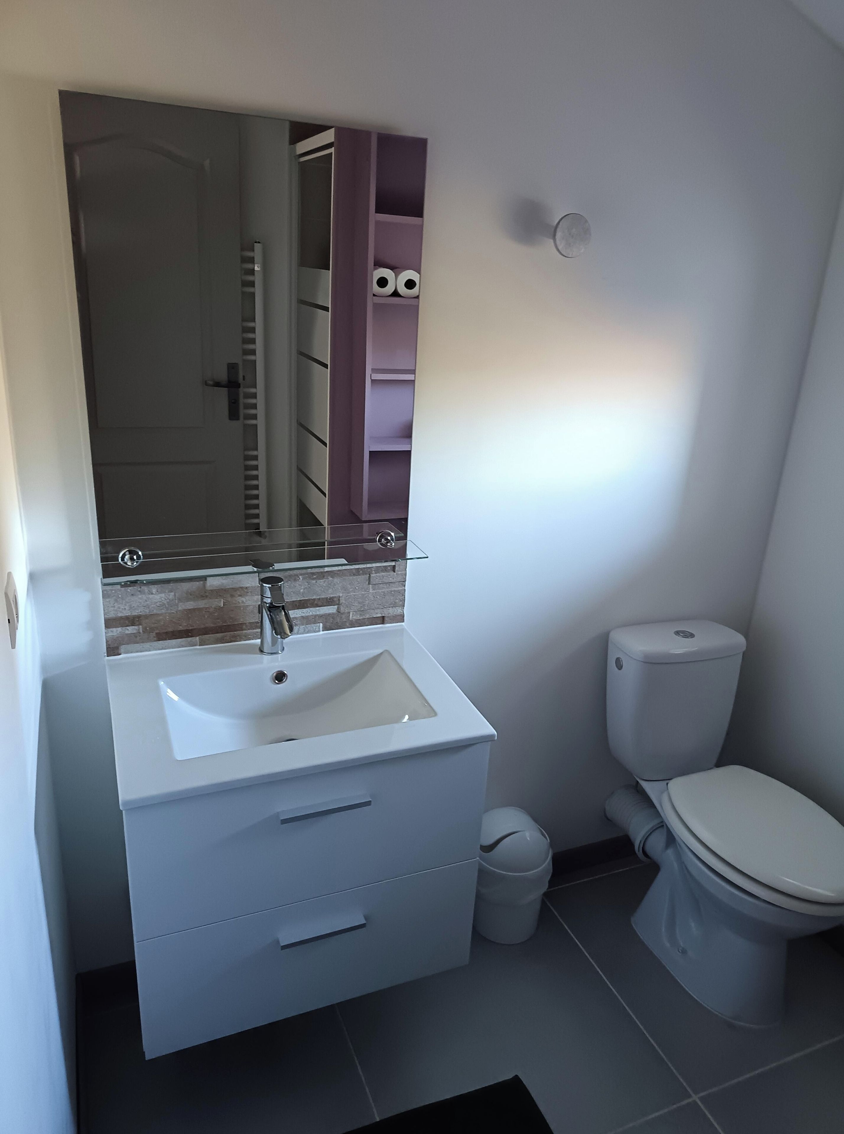 Une salle de bain avec un lavabo blanc, des toilettes et un miroir.
