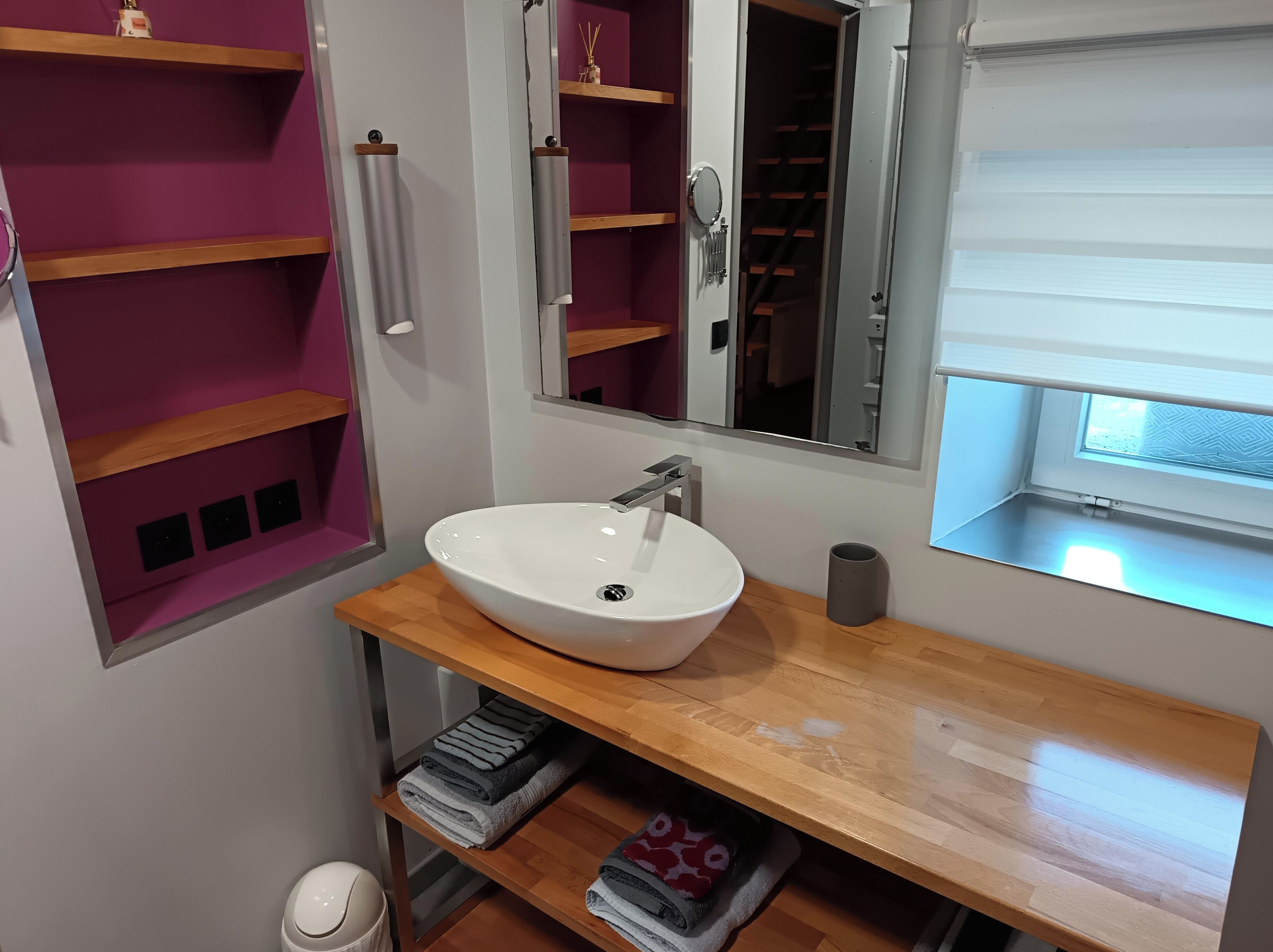 A bathroom with a white sink, wooden shelves, a mirror, and a window.