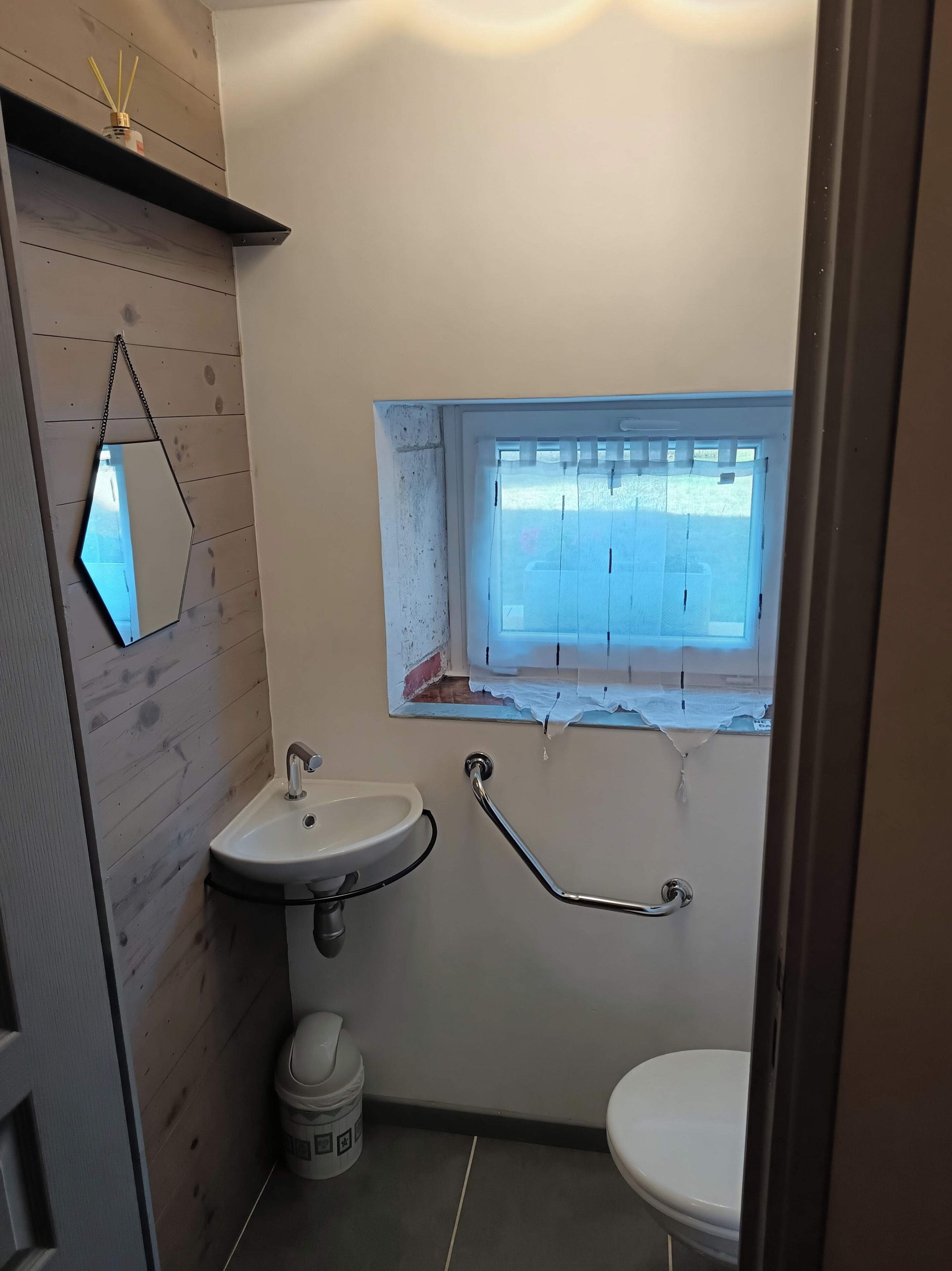 Une petite salle de bain avec un lavabo, des toilettes et une fenêtre donnant sur l’extérieur.