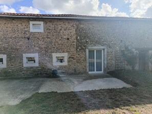 A stone building with a tiled roof, a door with glass panels, and a small window with a plant. - Vrbo Property (Terres-de-Haute-Charente)