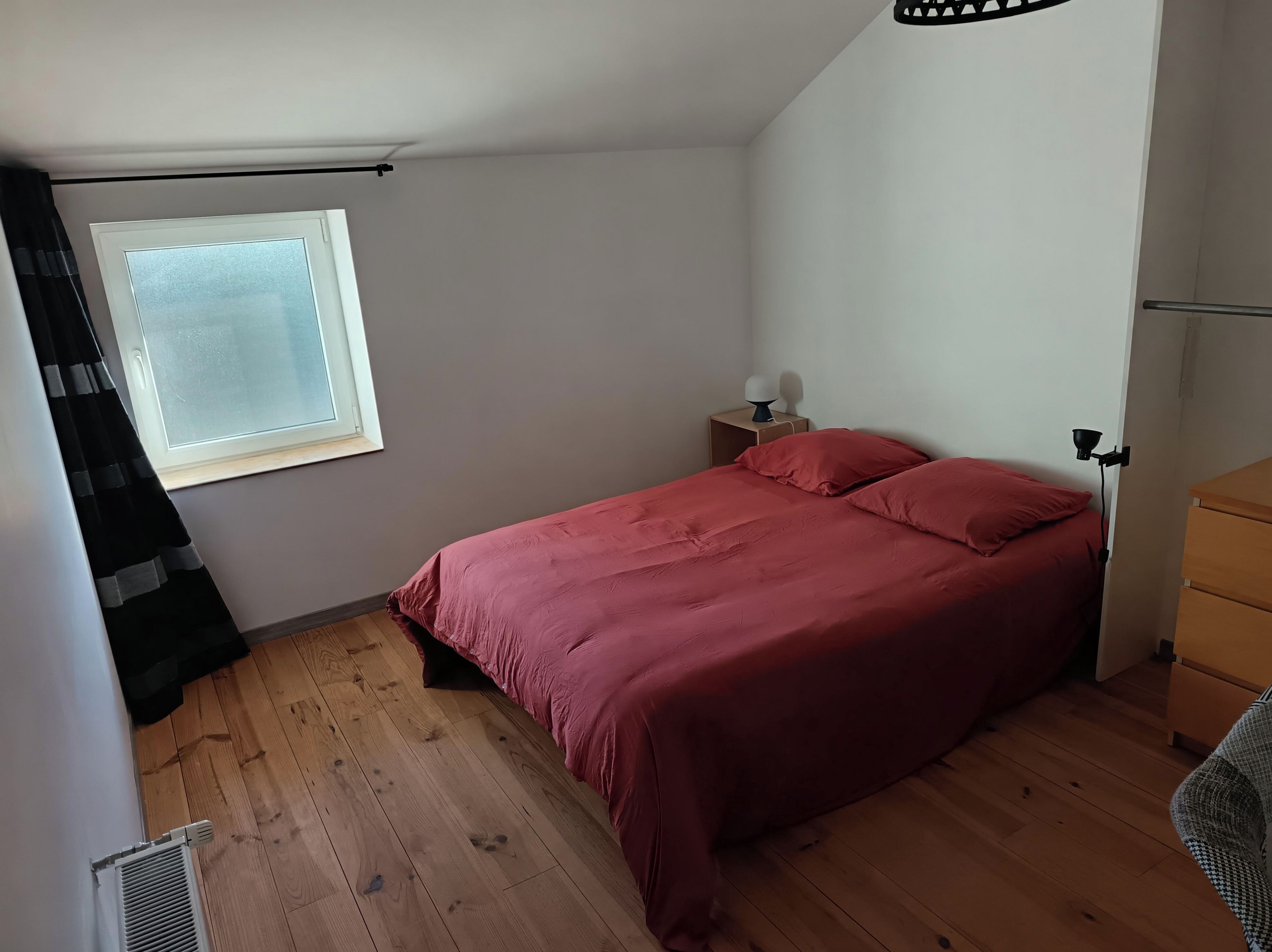 Een slaapkamer met een bed, nachtkastje, lamp, raam en radiator.