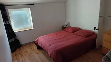 Een slaapkamer met een bed, nachtkastje, lamp, raam en radiator.