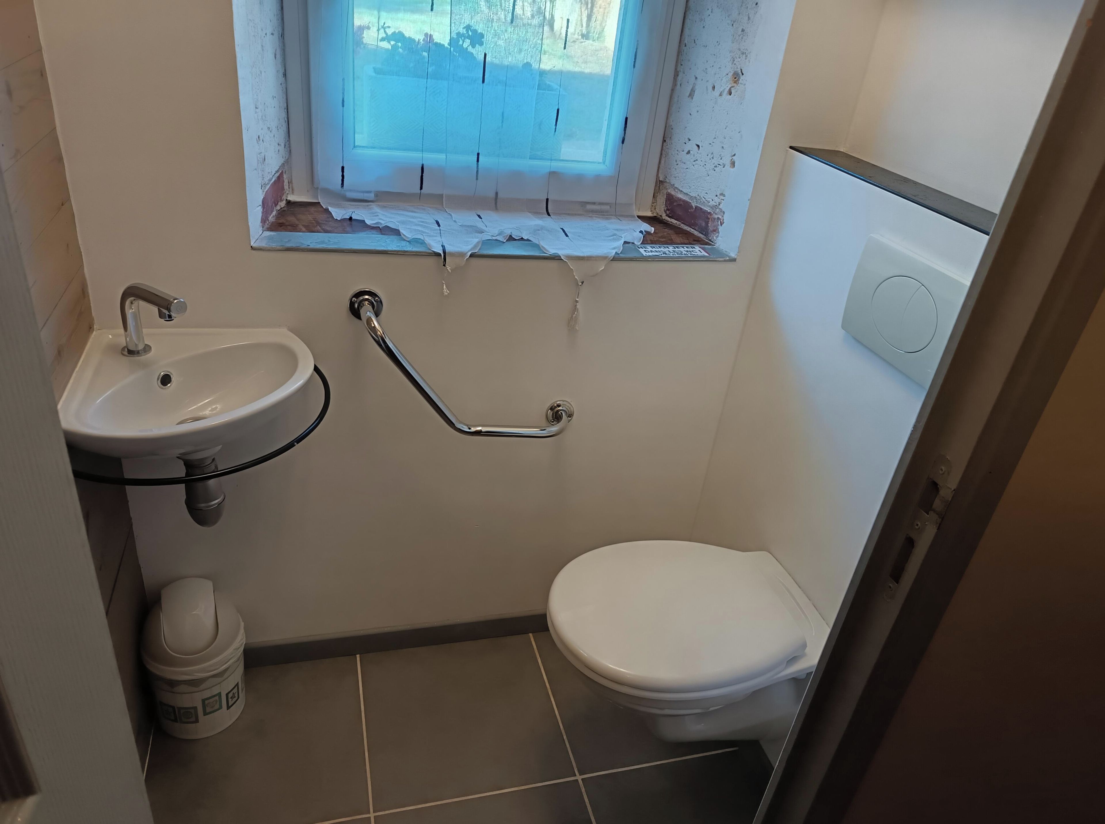 Une petite salle de bain avec un lavabo blanc, des toilettes et une fenêtre donnant sur l’extérieur.