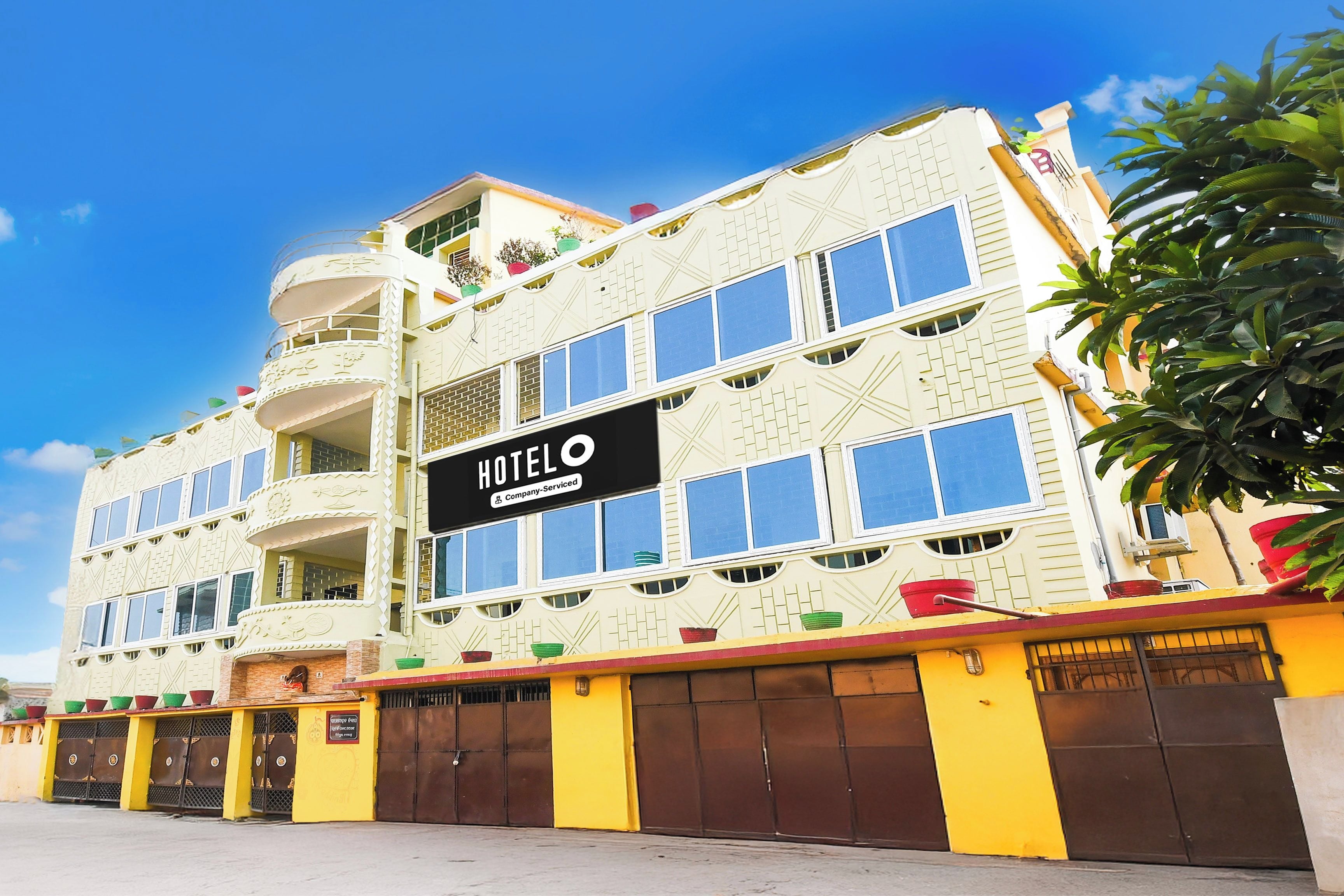 Un hotel con un cartel que dice 'HOTEL' y un logotipo con los servicios de la empresa. Tiene varios pisos con balcones y una fachada amarilla y marrón.