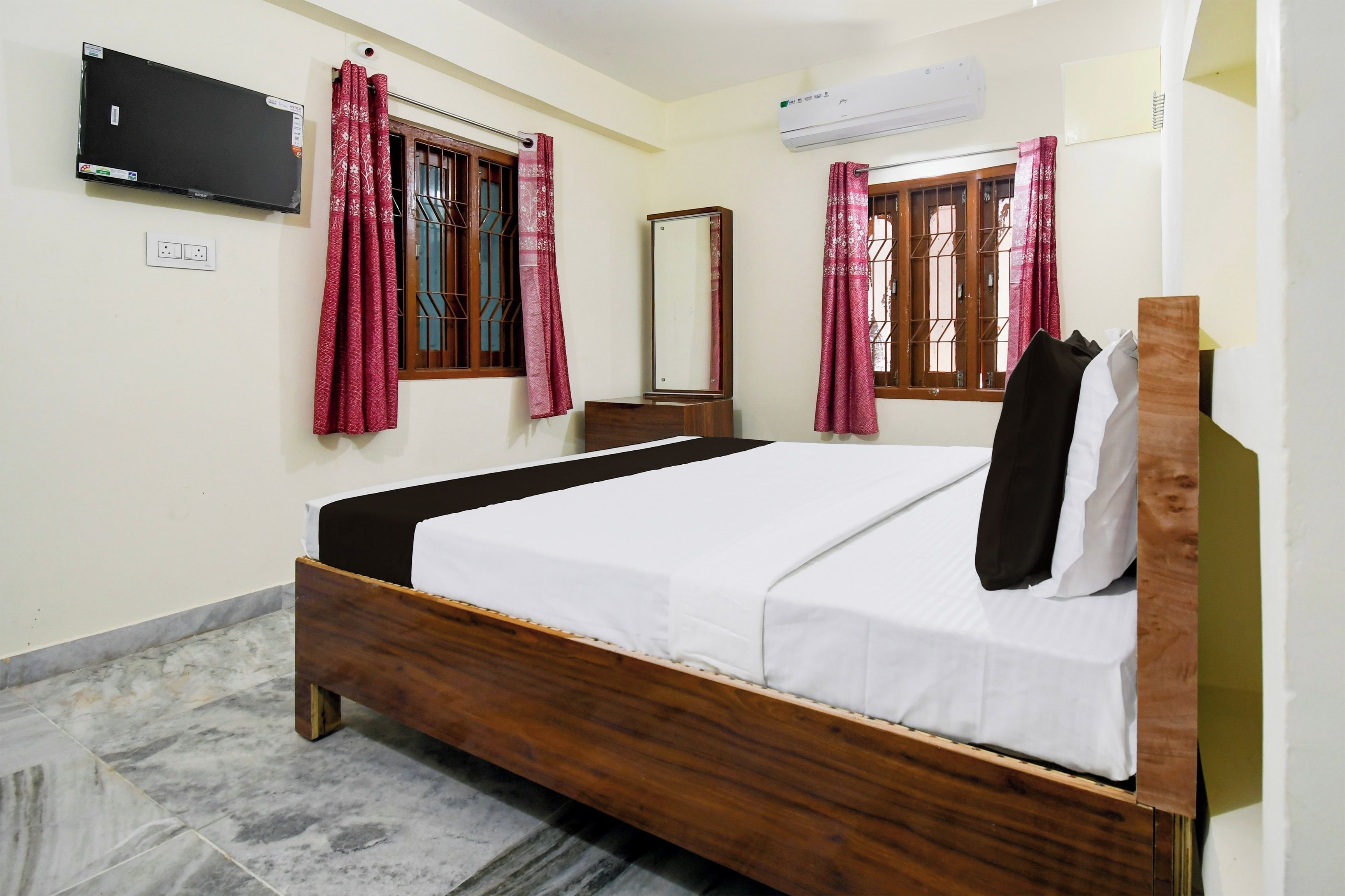 A bedroom with a bed, a flat-screen TV, an air conditioner, and a window with a curtain.