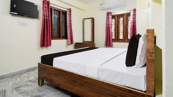A bedroom with a bed, a flat-screen TV, an air conditioner, and a window with a curtain.