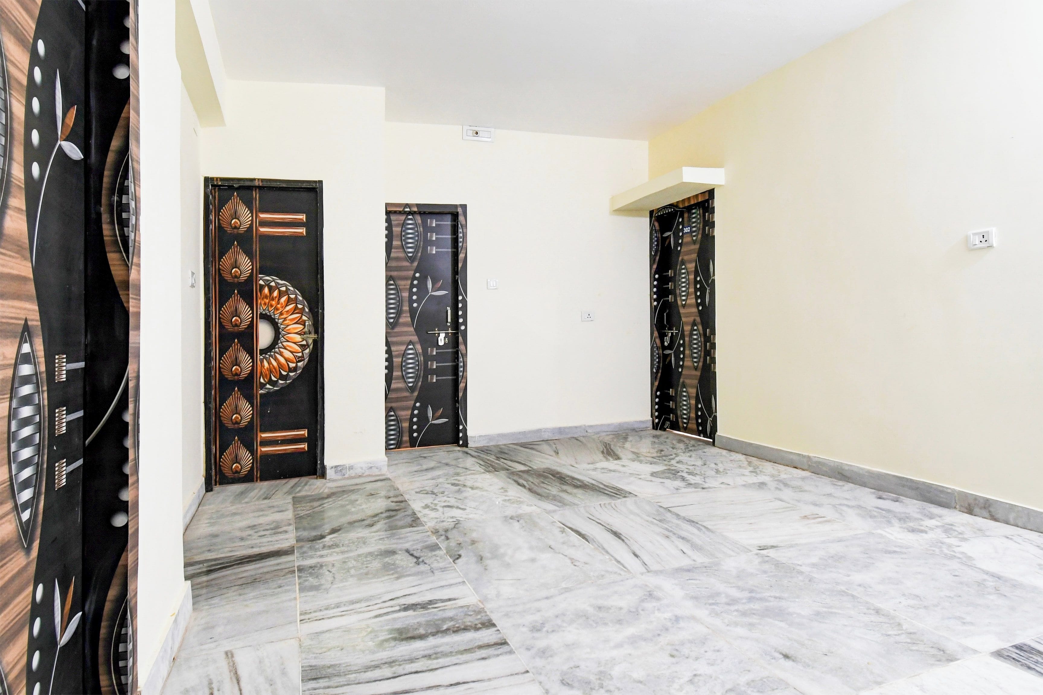 A hallway with three doors, each with a unique design, leading to rooms. The floor is tiled with a marble pattern.