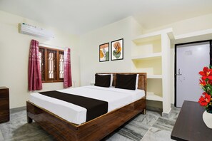 A hotel room with a wooden bed, a window with curtains, a wall-mounted air conditioner, and a door. - Super Hotel O Khandagiri (Bhubaneswar)