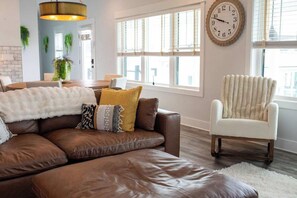 Ein Wohnzimmer mit einem braunen Ledersofa, einem weißen Sessel und einer großen Wanduhr.
