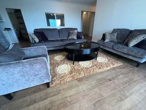 Ein modernes Wohnzimmer mit einer Eckcouch, einem runden Couchtisch und einem gemusterten Teppich.