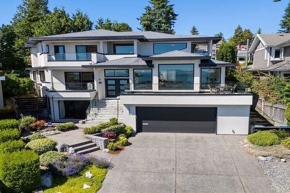 Ein modernes, zweistöckiges Haus mit Garage, überdachter Terrasse und gepflegtem Garten.