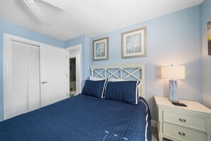 A bedroom with a bed, a nightstand, a lamp, and two framed pictures on the wall. - Block from the Beach – Pristine Avalon Condo Just One Block from the Beach! (Avalon)