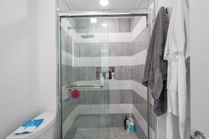 Een moderne badkamer met een douchecabine, toilet en een handdoekrek met handdoeken.