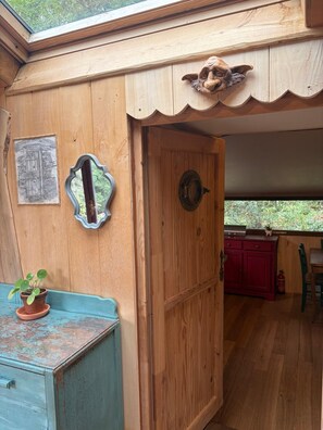 A wooden interior with a door, a small table with a plant, and a view through a window.