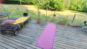 A wooden deck with a yoga mat, a lounge chair, a small table, and potted plants.