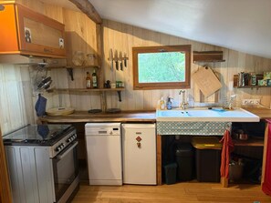 A compact kitchen with wooden cabinets, a built-in oven, a refrigerator, and a window above the sink.