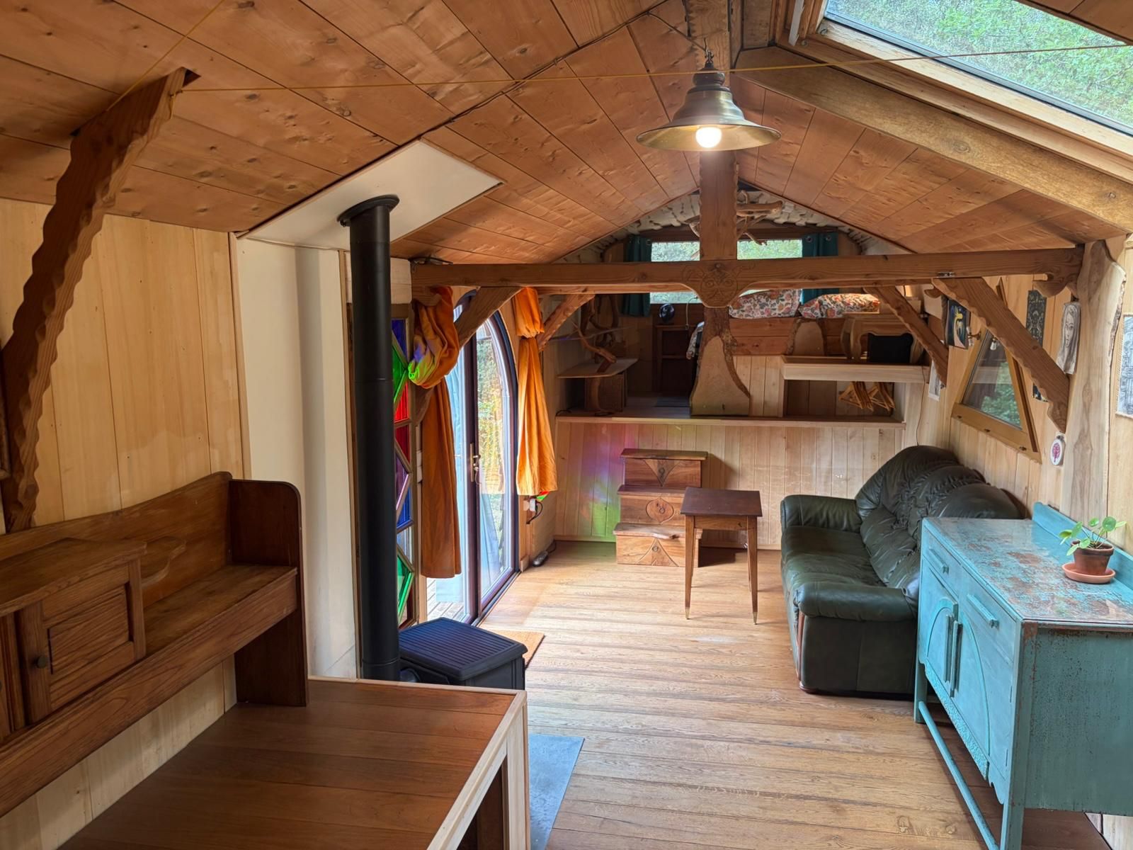 Een gezellig houten interieur met een bankje, een slaapbank, een tafel en een rustiek plafond.
