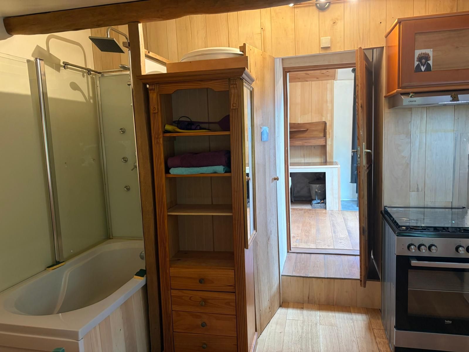 A compact kitchen with a built-in oven, a wooden cabinet with open shelves, and a bathtub.