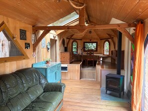 A cozy cabin interior with a wooden ceiling, a sofa, a desk, and a fireplace.