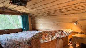 Une chambre de cabine comprenant un lit, un bureau, une lampe et une fenêtre avec des rideaux.