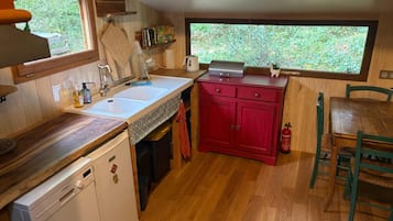 A compact kitchen with a dishwasher, a sink, a red cabinet, and a window with a view of greenery.
