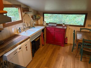 A compact kitchen with a dishwasher, a sink, a red cabinet, and a window with a view of greenery.