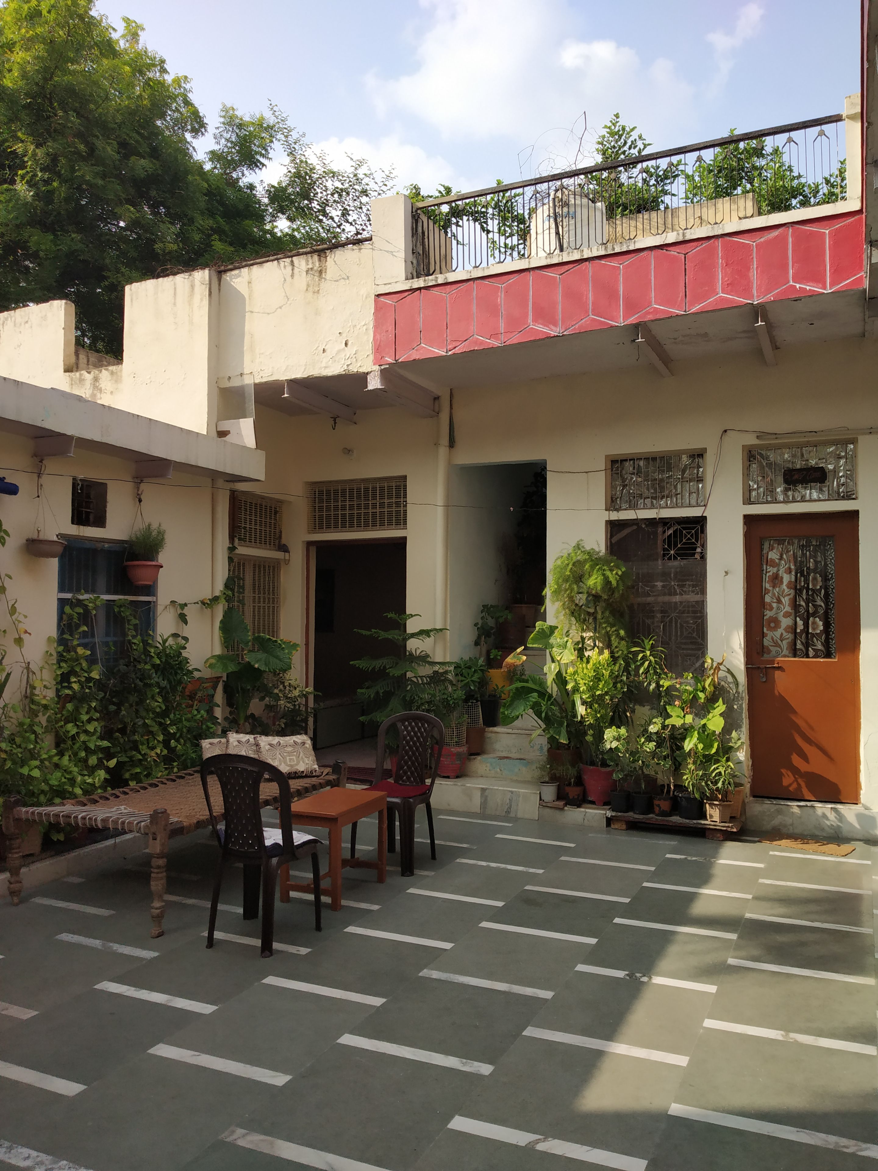 A courtyard with a seating area, potted plants, and a building with a red balcony.