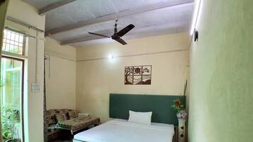 A room with a bed, a ceiling fan, a wall-mounted artwork, and a potted plant.