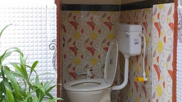 A small, enclosed bathroom with a toilet, a water tank, and a potted plant.