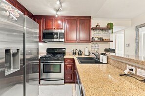 Eine Küche mit Edelstahlgeräten, Holzschränken und Arbeitsplatten aus Granit, inklusive eingebauter Mikrowelle.