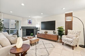 A modern living room with a fireplace, a flat-screen TV, a sofa, a coffee table, and a patterned armchair. - Stylish 3BR Woodland Hills with Private Balcony (Los Angeles)
