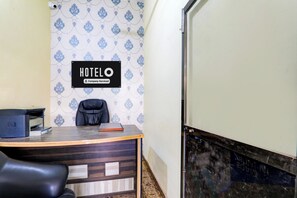 A hotel reception desk with a sign indicating it's company-serviced, a printer, a leather chair, and a patterned wallpaper. - Super Hotel O Sudhirpur (Varanasi)