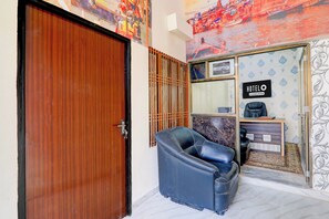 A hotel reception area with a reception desk, a reception sign, a reception door, and a blue leather chair. - Super Hotel O Sudhirpur (Varanasi)
