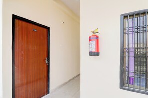 A wooden door with a number plate, a fire extinguisher mounted on a wall, and a barred window. - Super Hotel O Sudhirpur (Varanasi)