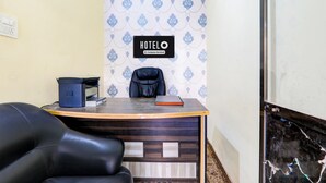 Un comptoir d’accueil d’hôtel avec un panneau indiquant qu’il est géré par l’entreprise, un fauteuil en cuir noir et une imprimante.