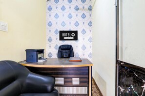 A hotel reception desk with a sign indicating it's company-serviced, a black leather chair, and a printer. - Super Hotel O Sudhirpur (Varanasi)